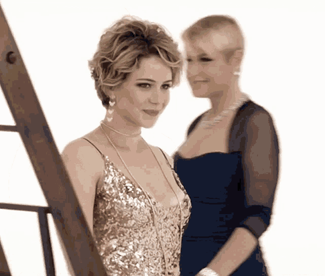 two women standing next to each other with one wearing a gold dress and the other a blue dress