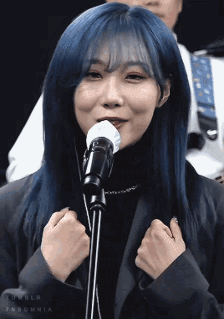 a woman with blue hair is singing into a microphone .