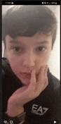 a young boy wearing a black ea7 shirt is taking a selfie on his phone .