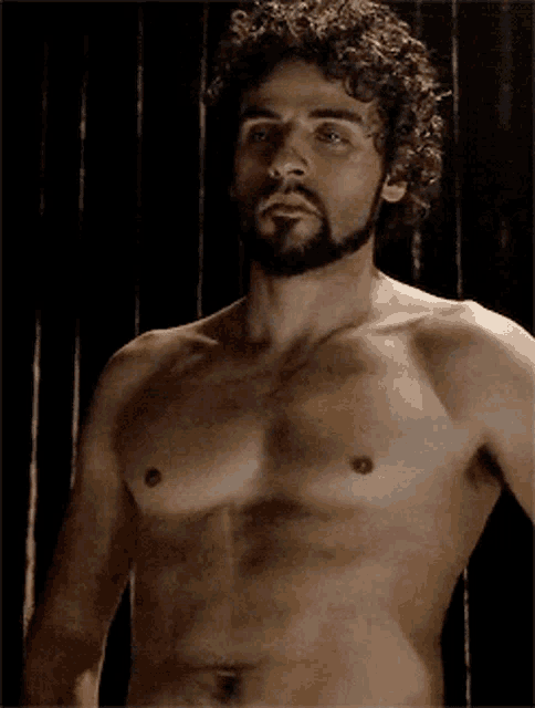 a shirtless man with a beard stands in front of a black wall