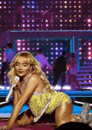 a woman in a yellow dress is kneeling on the floor while holding a microphone on a stage .