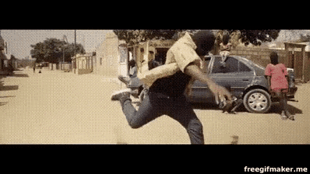 a man in a mask is running down a dirt road in front of a car .