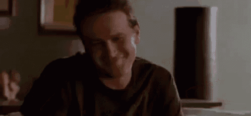 a man in a black shirt is sitting at a table with his hands outstretched and says `` oh well '' .