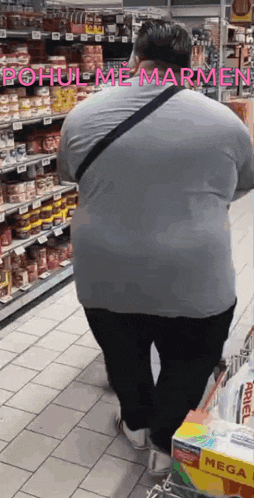 a man in a grey shirt is walking down a grocery store aisle with a mega box in front of him .