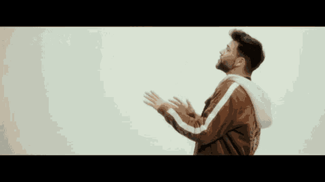 a man with a beard is wearing a brown jacket and a white hoodie .