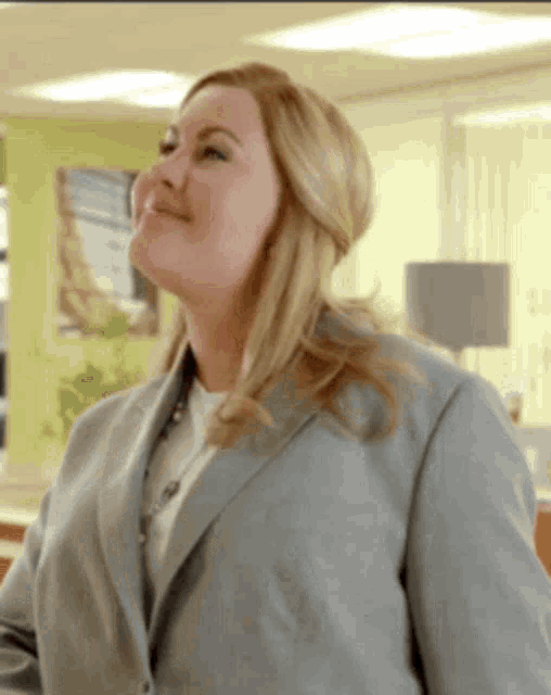 a woman in a grey suit is smiling in a room