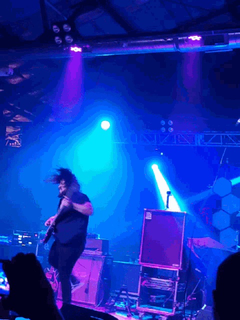 a man singing into a microphone on a stage with a purple light behind him
