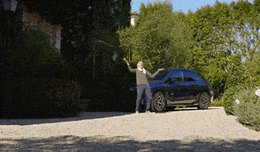 a man is standing in front of a black car with his arms outstretched