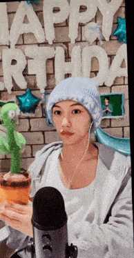 a person wearing a blue hat is holding a cactus in front of a sign that says happy birthday