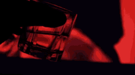 a close up of a person pouring a drink into a glass with a red background