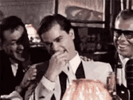 a man in a suit and tie is covering his mouth while sitting at a table with other men .