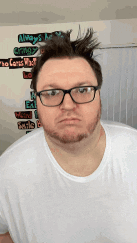 a man wearing glasses and a white shirt is standing in front of a wall that says " always be okay "