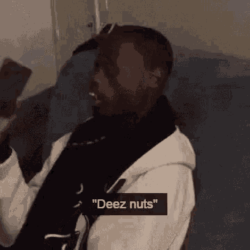 a man is sitting on a couch holding a cell phone in his hand and says `` deez nuts '' .