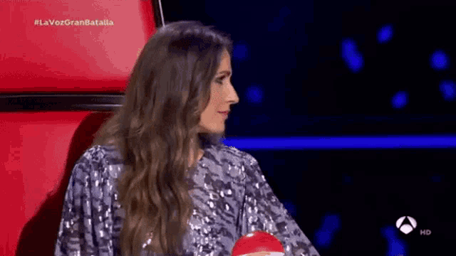 a woman in a sequined dress is sitting in a red chair on a stage .