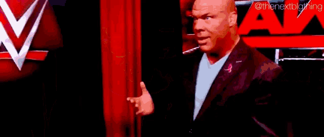 a bald man in a suit and tie is standing in front of a raw sign .