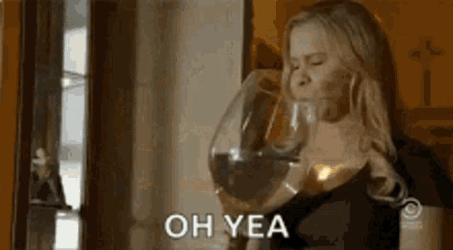 a woman is drinking a glass of red wine and saying oh yea .