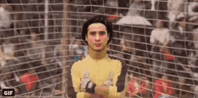 a soccer goalie with his arms crossed is standing in front of a soccer net .