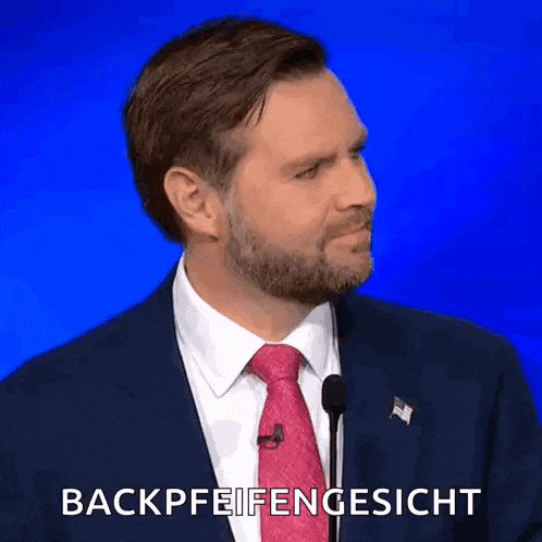 a man in a suit and tie is speaking into a microphone and says backpfeifengesicht