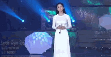 a woman in a white dress is singing into a microphone while holding an umbrella .