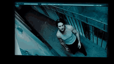 a man in a white tank top is walking down stairs in a dark room
