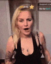 a woman with blonde hair and a tattoo on her chest is wearing a black tank top with a plunging neckline .