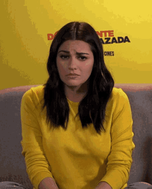 a woman in a yellow sweater sits on a couch in front of a yellow wall that says delante azada