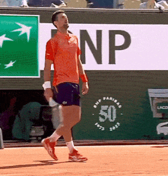 a man in an orange shirt is holding a tennis racquet in front of a bnp sign