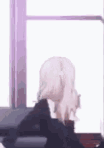 a girl is standing in front of a window with her head in her hands .