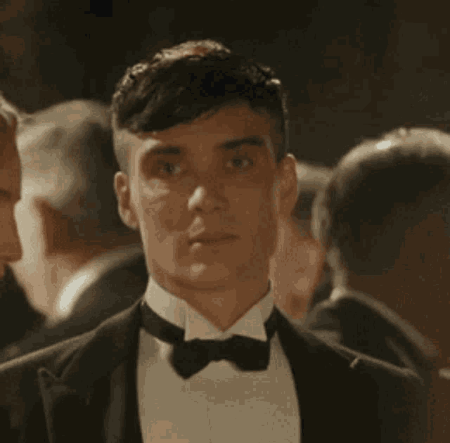 a man in a tuxedo and bow tie is standing in a crowd .
