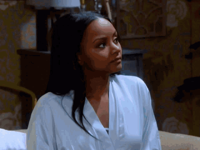 a woman wearing a white robe is sitting on a bed