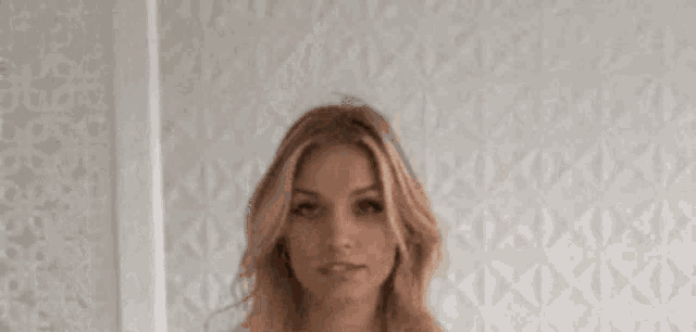 a woman is standing in front of a white wall and looking down .