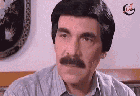 a man with a mustache and a wig on his head is looking at the camera .