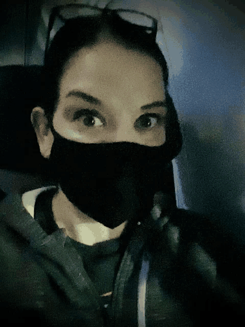 a woman wearing a black face mask and glasses looks at the camera