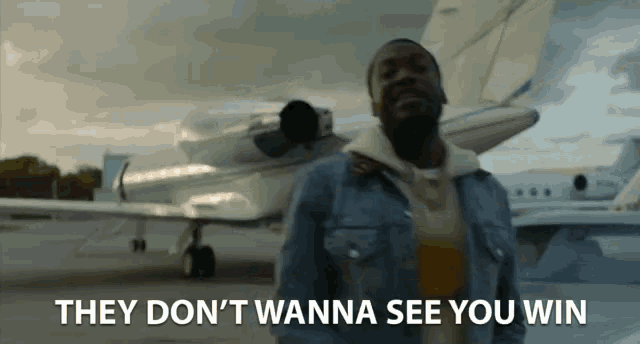 a man standing in front of a plane with the words they don 't wanna see you win behind him