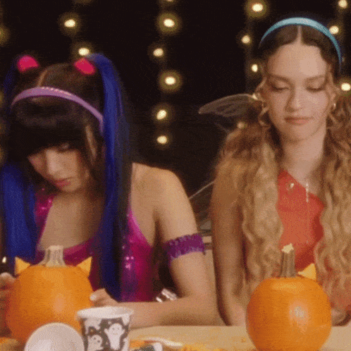two women sitting at a table with pumpkins and cups