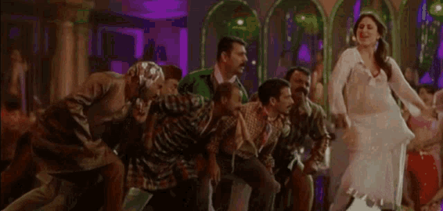 a woman in a white dress is dancing with a group of people sitting around her .
