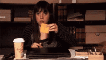 a woman sitting at a desk with a cup of coffee and a piece of cheese in her hand