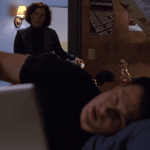 a man is looking at a laptop while a woman stands behind him in a room