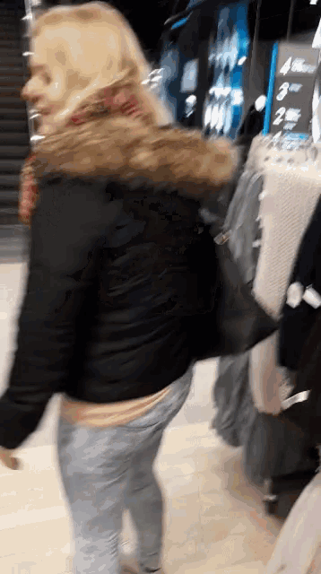 a woman in a black jacket with a fur hood walks through a store