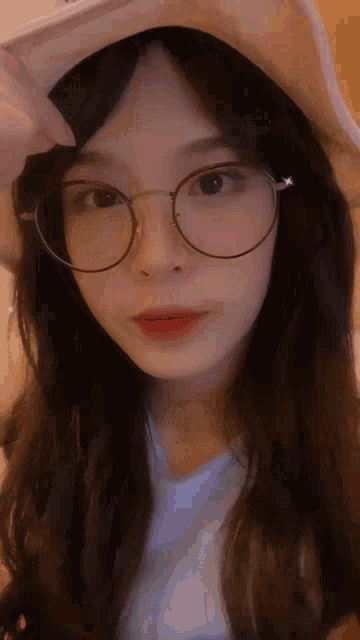 a young woman wearing glasses and a hat looks at the camera