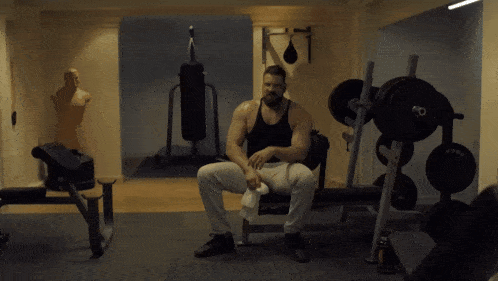 a man sits on a bench in a gym with a bottle of water on his lap