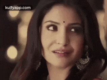 a close up of a woman 's face with a bindi on her forehead and earrings .