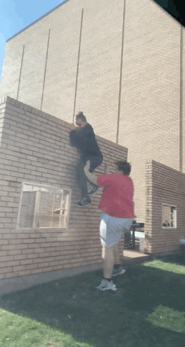 a woman in a red shirt is helping another woman climb a brick wall