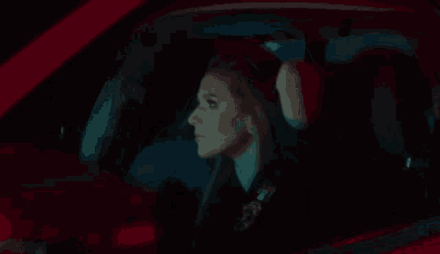 a woman is driving a red car at night .