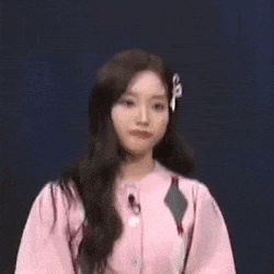 a woman in a pink shirt is standing in front of a microphone and looking at the camera .