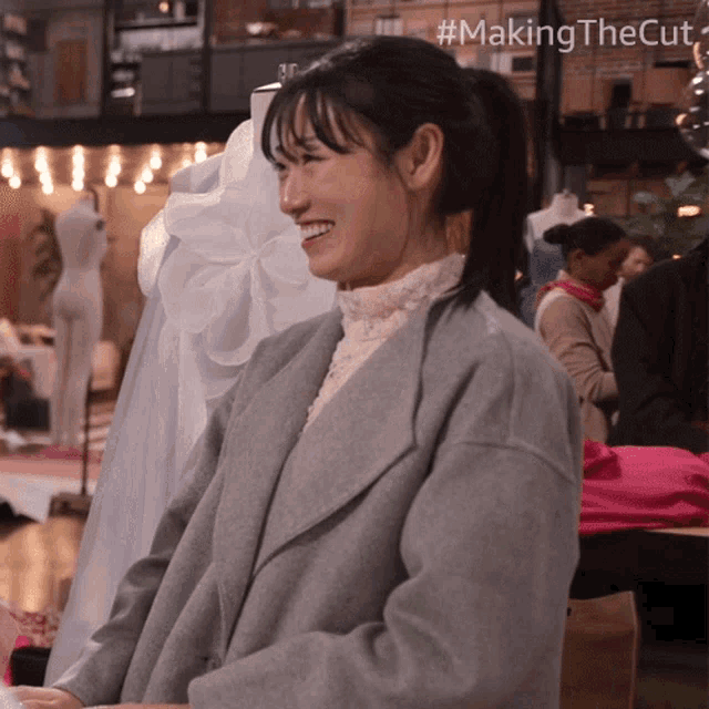 a woman in a grey coat is smiling in front of mannequins with the hashtag #makingthecut