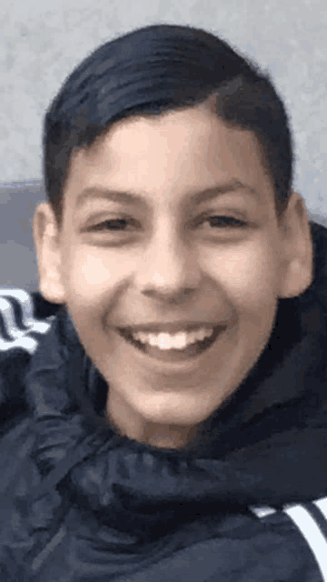 a young boy wearing a black jacket with white stripes is smiling for the camera