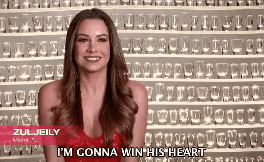 a woman in a red dress says i 'm gonna win his heart in front of a wall of shot glasses