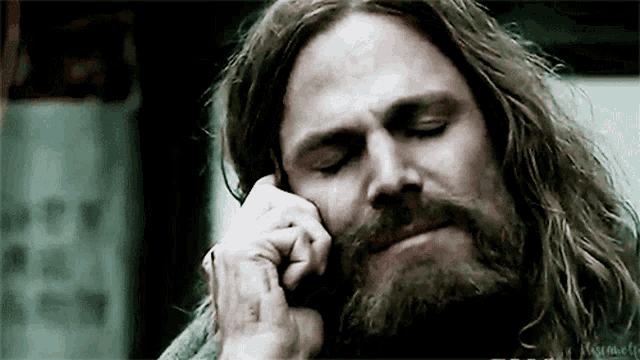 a man with long hair and a beard talking on a cell phone .