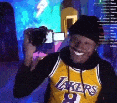 a man in a lakers jersey is taking a picture with a camera .